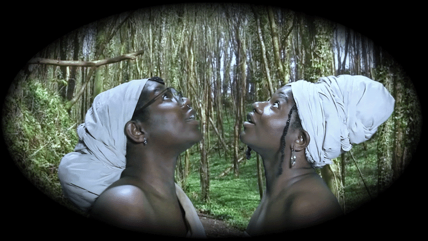 Two women face each other, they are wearing white turbans. They look upwards. In the background is a wooded landscape.