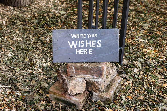 On a stack of bricks there is a sign displayed that reads 'Write your wishes here' on a chalkboard.