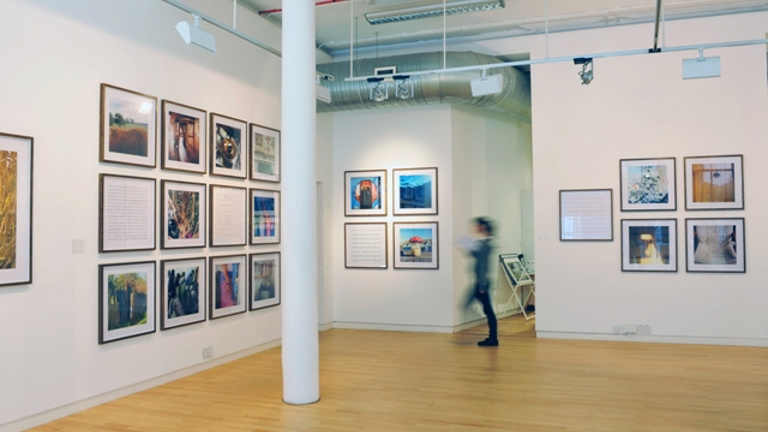 installation view of a gallery space with multiple square framed photographs on the walls.