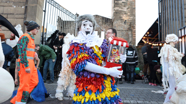 Performers dressed in circus costume in front of a large gate 