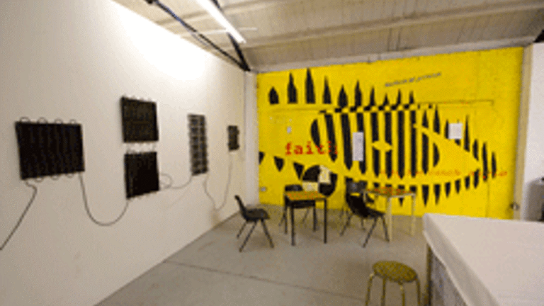 Gallery installation, mounted screens on wall, chairs and tables, graphic eye design 