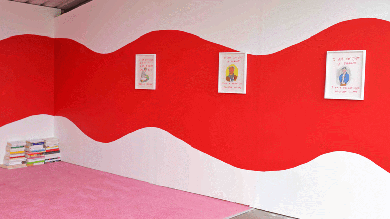 a wide red squiggle painted on a gallery wall. Small framed drawings hung on the wall. A pink carpet and pile of books