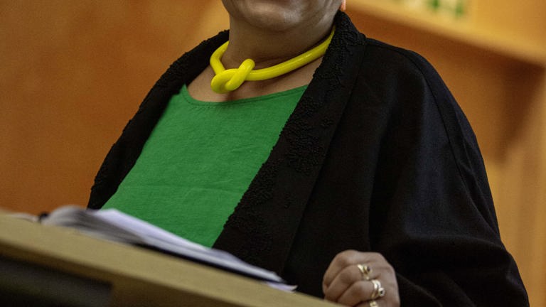 close up of a person wearing green and black standing at a lectern smiling