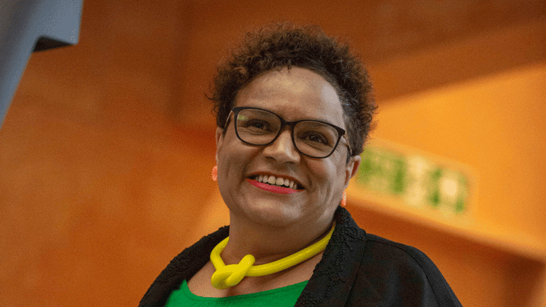 close up of a person wearing green and black standing at a lectern smiling