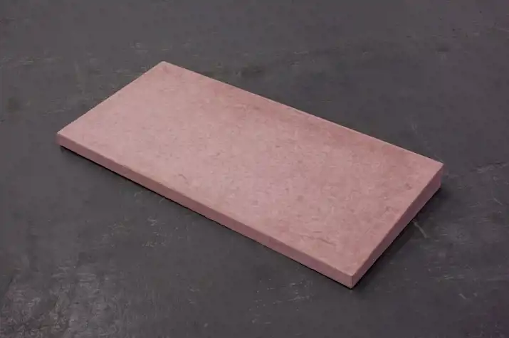 Rectangular abstract sculpture cast in pink concrete with a slight incline sits on a grey floor
