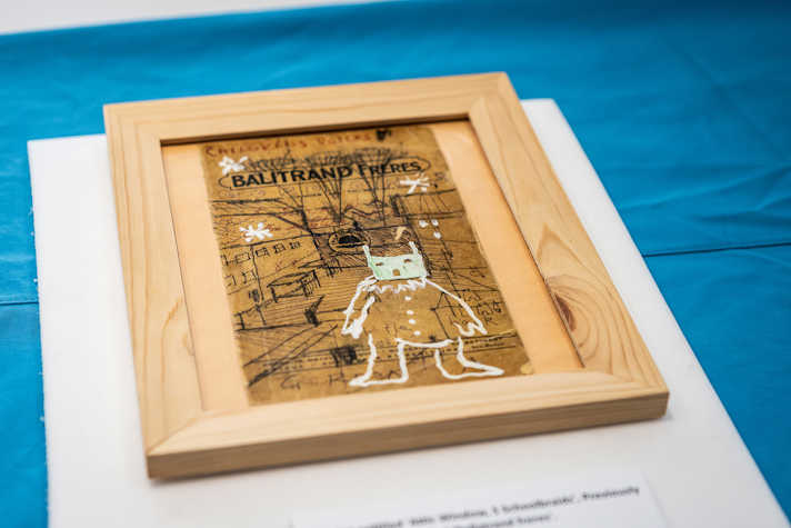 A drawing framed in a wooden frame displayed on a table covered by a blue tablecloth.