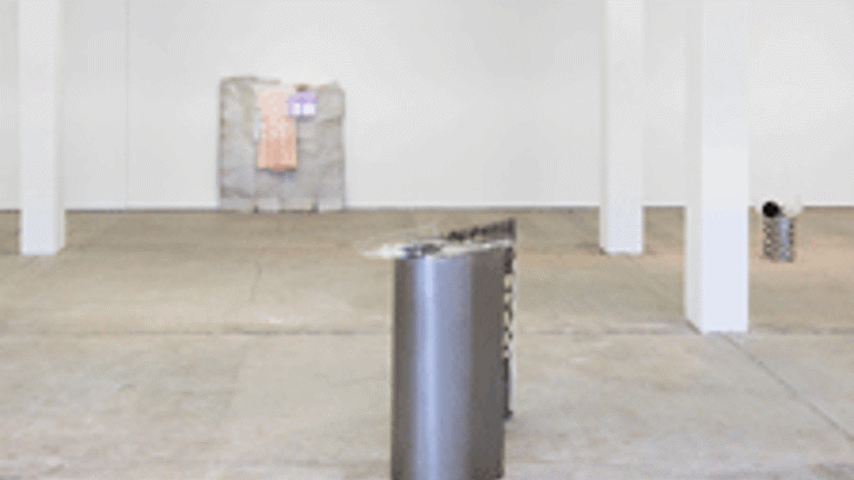 A white gallery space with columns and a metal sculptural work in the foreground. Another sculptural work is visible in the background 