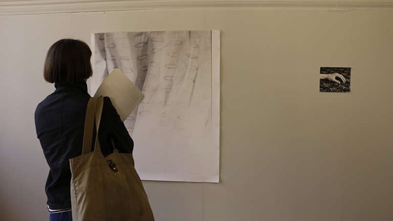 Gallery installation, hung print and photograph showing a hand, festival attendee viewing the work