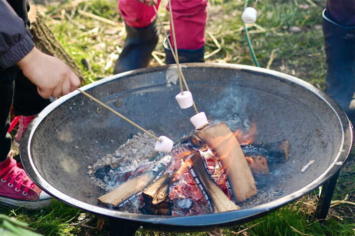 Hands roasting marshmallows over a steel fire pit