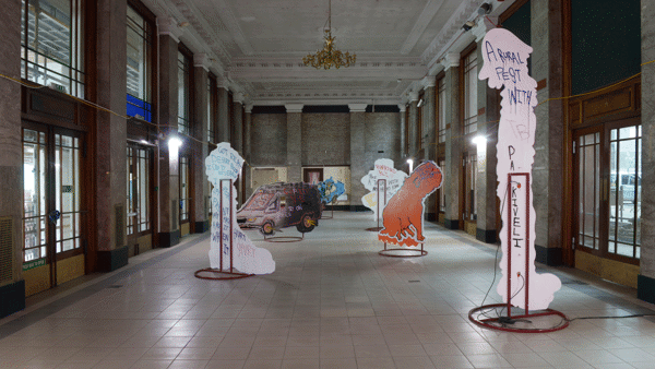 Six plywood boards held by a metal base displayed along the room facing different directions with drawings on them and in the reverse part they have handwritten text in Kelvin Hall as a part of Glasgow International 2018.