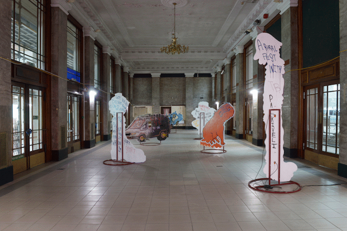 Six plywood boards held by a metal base displayed along the room facing different directions with drawings on them and in the reverse part they have handwritten text in Kelvin Hall as a part of Glasgow International 2018.