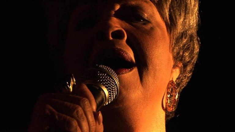 dim and warmly lit close up of someone singing into a microphone