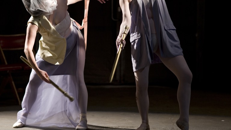 two people in dancelike motion both wearing mesh bags on their heads and holding sticks