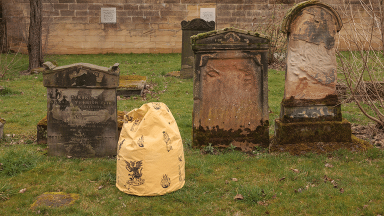 A photograph of a grave yard with a row of grave stones, and a yellow sculptural object in the middle