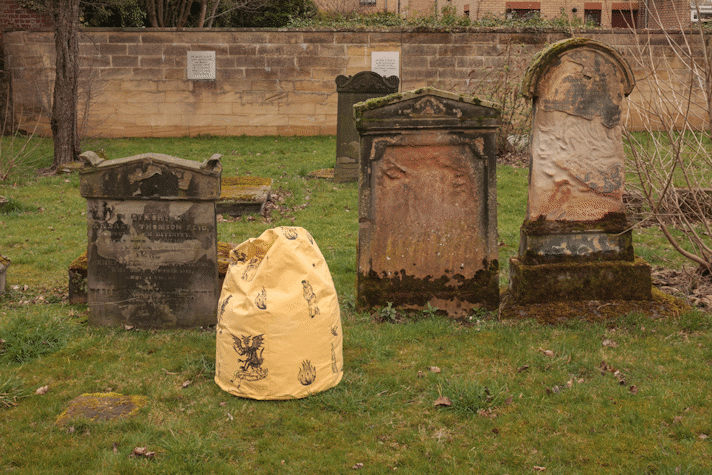 A photograph of a grave yard with a row of grave stones, and a yellow sculptural object in the middle