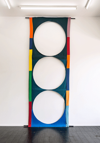 The image shows an artwork that is a textile hanging with three large circles cut out