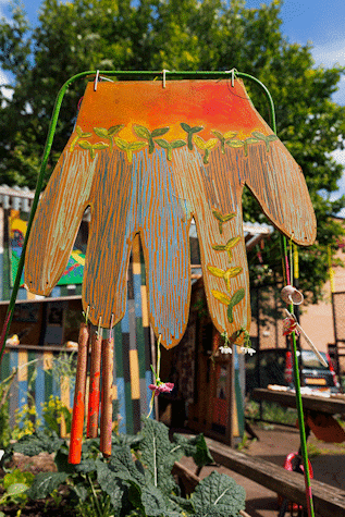 An artwork of a hand hangs from a wire frame, above plants below.