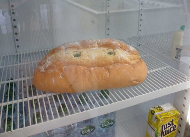A loaf of bread in a fridge with two eyes inserted in it.