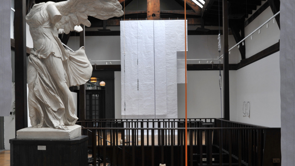 white sheets of fabric hanging from a wood beamed ceiling. their is a winged headless marble statue in front