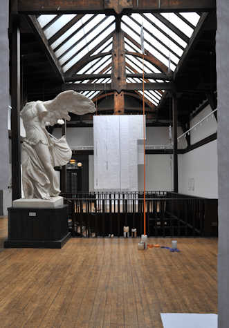 white sheets of fabric hanging from a wood beamed ceiling. their is a winged headless marble statue in front