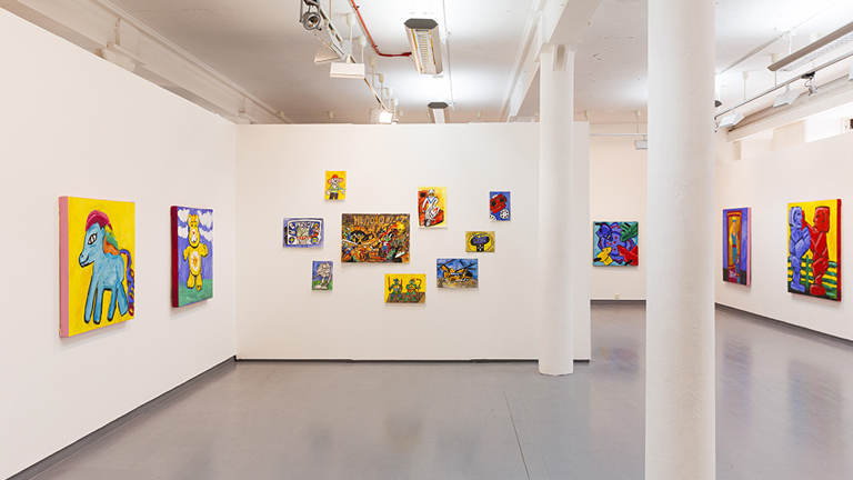 Colourful artworks are displayed on white walls in a gallery space.