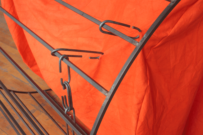 Close up view of sculptural work including metal structure and orange material