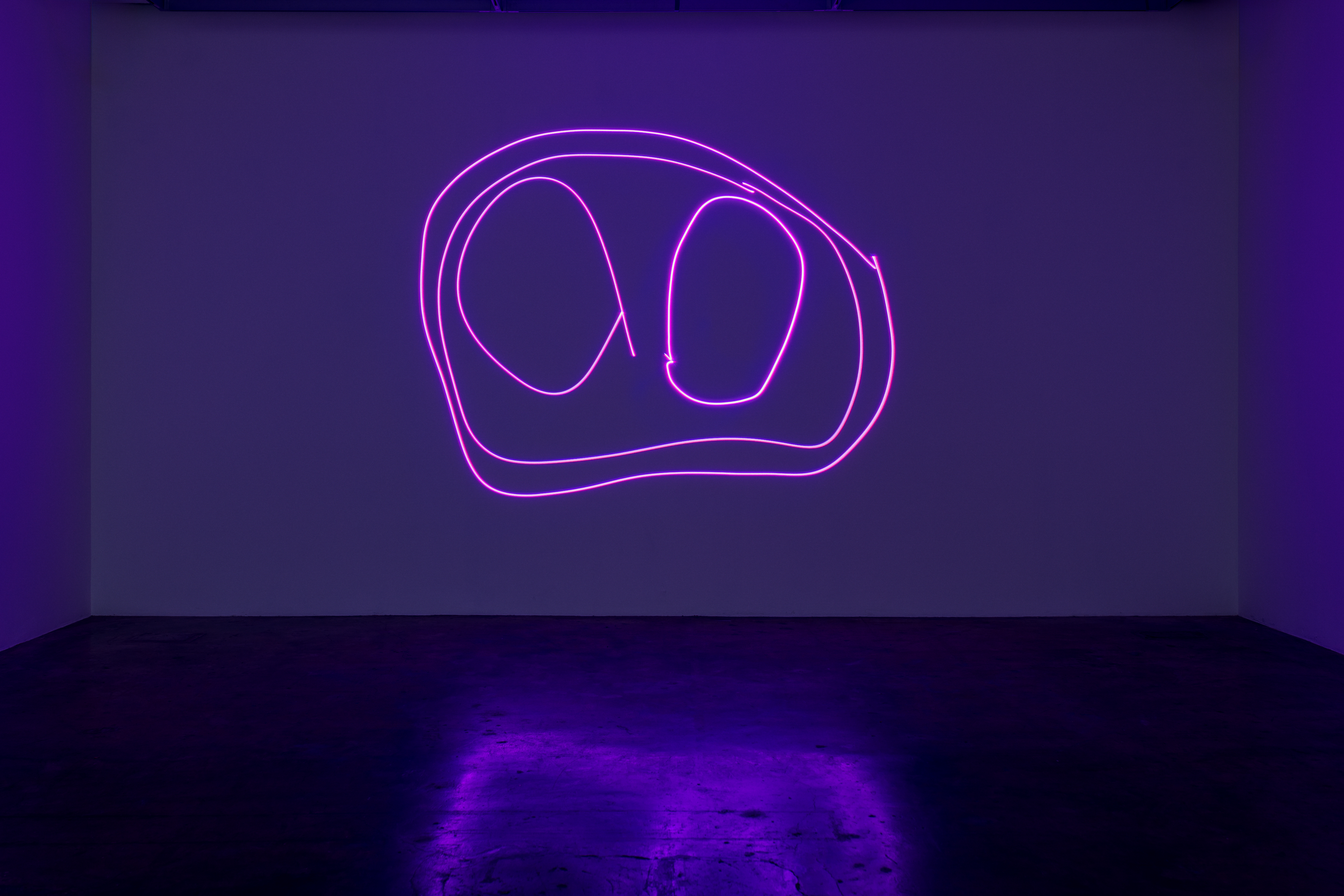 A dark room with a purple hue, projected in the centre is a neon purple childrens drawing. The drawing features a circular shape with eyes 