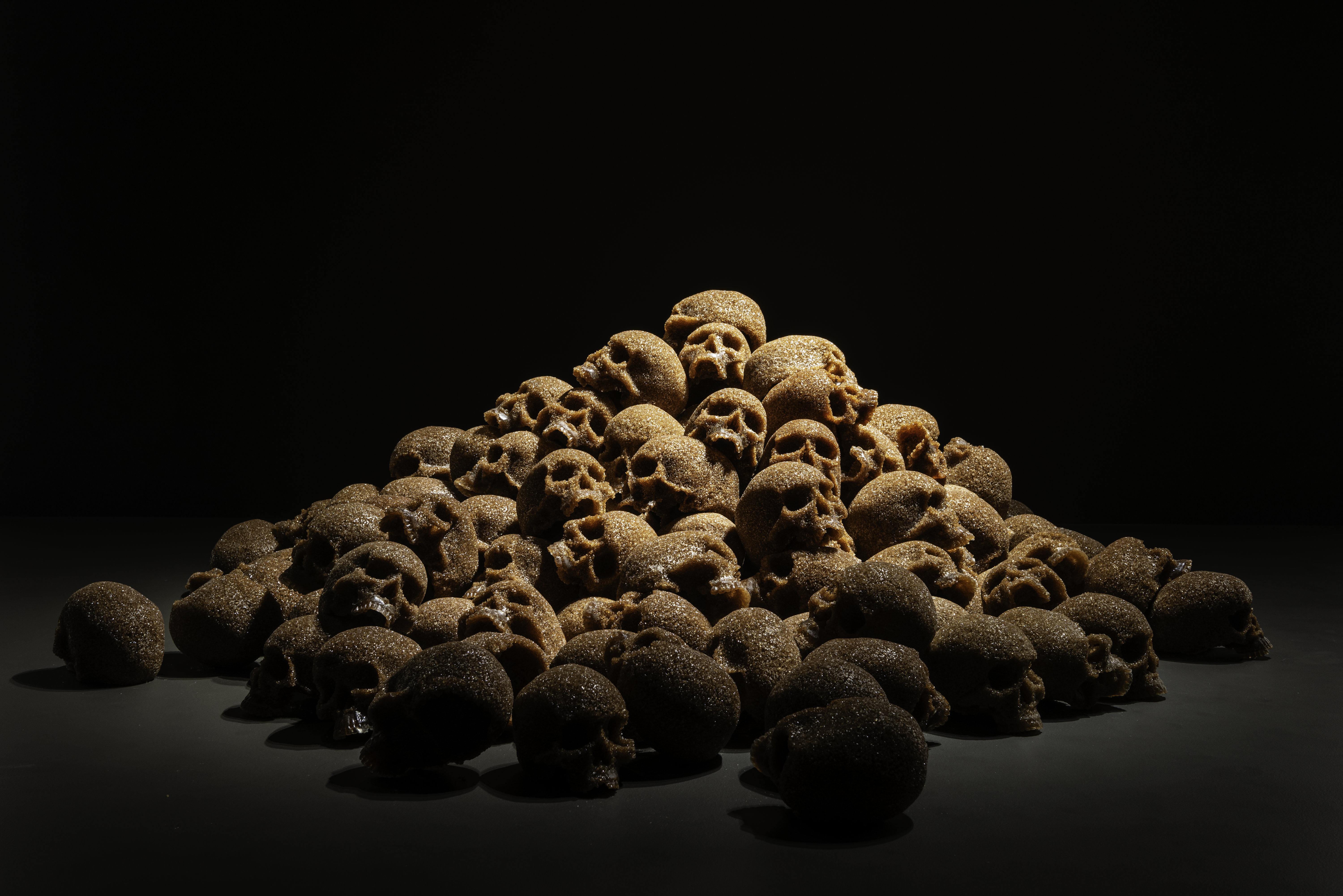 Skulls made from unrefined sugar mounted upon one another against a black backdrop on the ground