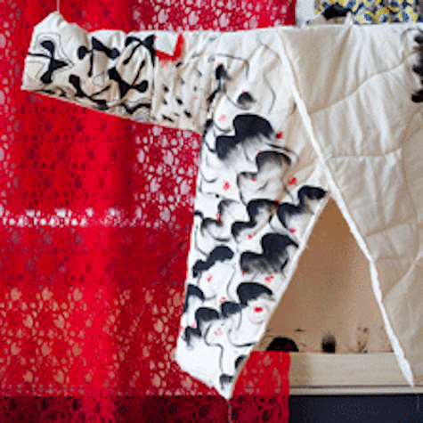 Large white jacket like garment suspended on a pole, with black graphic on one side. A red curtain is hanging behind.