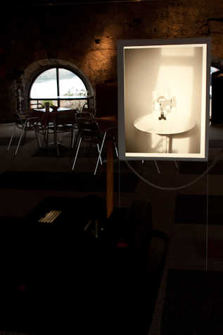 dark stone room with a circular window in the bag. in front is an illuminate photograph of a white table with a white object on top