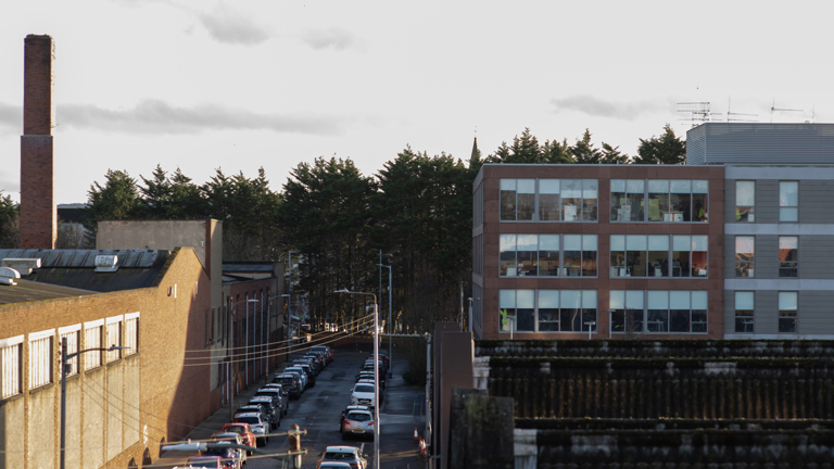 View from a rooftop looking down a street with an office building and trees in the distance. 