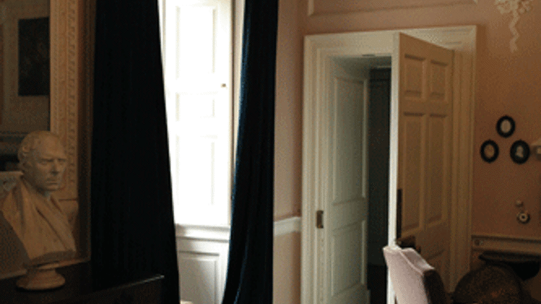 Interior shot of Pollok House, window with draped curtains, door, furniture including a chair, bust and hung paintings