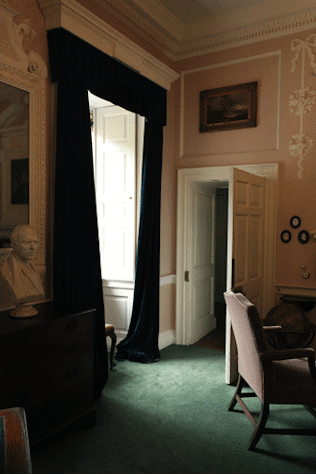 Interior shot of Pollok House, window with draped curtains, door, furniture including a chair, bust and hung paintings