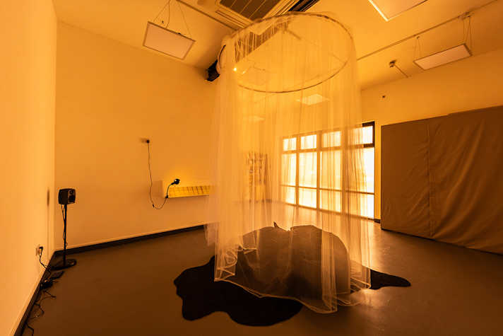 In the centre of a room, there is a canopy of fabric covering a pile of dark fabric.