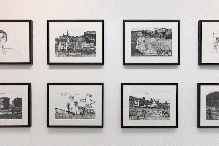 eight intricate pen drawings in black frames hang on a white wall