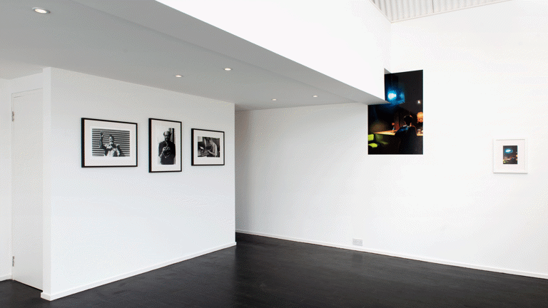 A white-walled exhibitions spaces with photographs on the floor