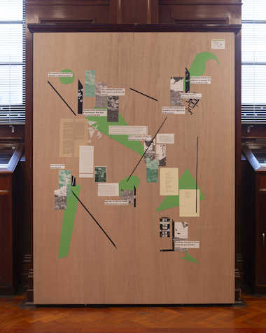 A large piece of MDF with images and writing on it, against bookcases.
