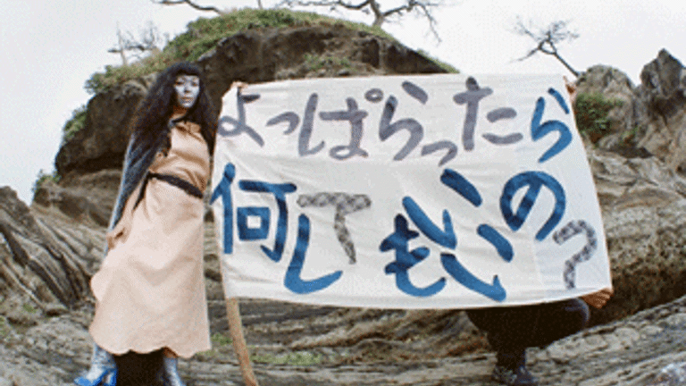 film still - an individual painted in blue holding a banner in front of a landscape