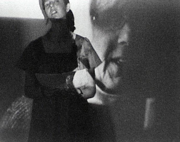 black and white image of a person standing infant of a projection on a wall of another persons face close up.