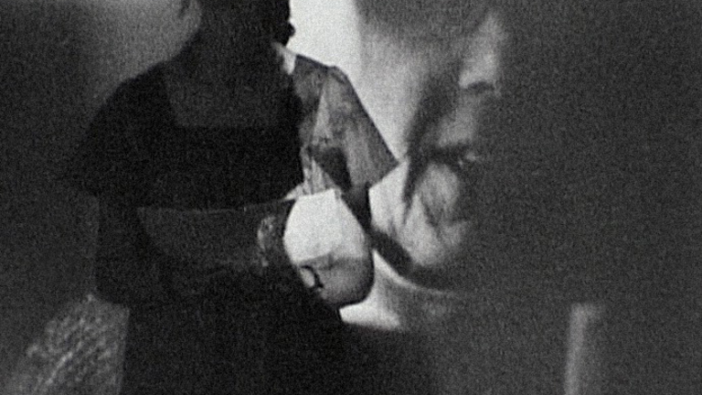 black and white image of a person standing infant of a projection on a wall of another persons face close up.