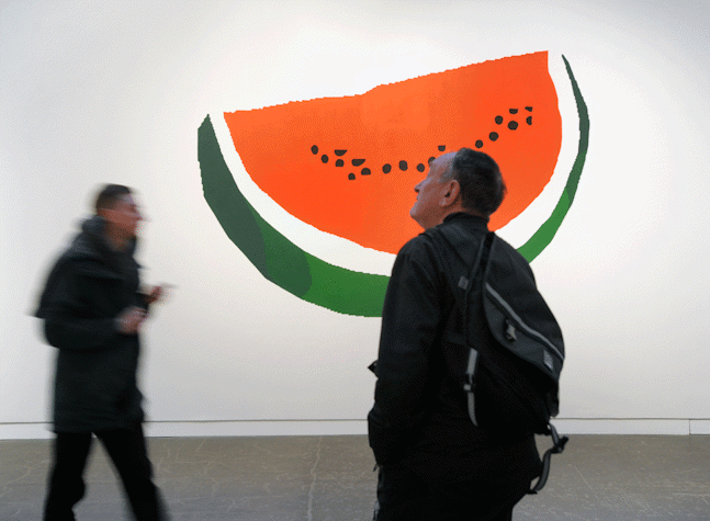 large painting of watermelon slice, with festival attendees viewing