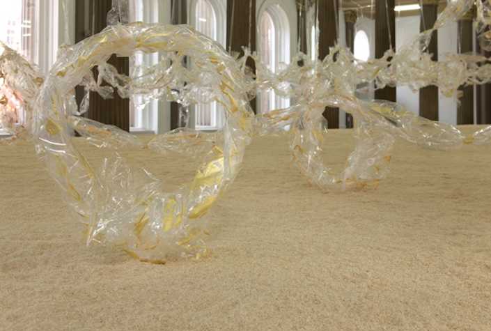 close up of sculptures made from cellophane with gold painted details on a bed of sand