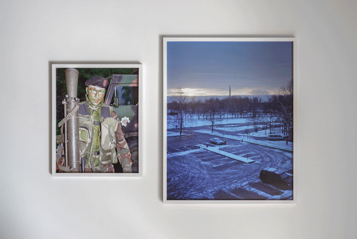 Two framed photographs are placed centrally side by side, the one on the left shows a man dressed in military gear holding a bazooka and the right one shows an aerial view of a snow covered parking lot.