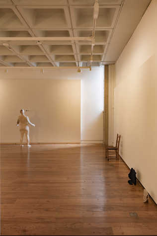 In a white wall, there is a white figurine at the back of the room, with a chair and other objects on the right side of the room.