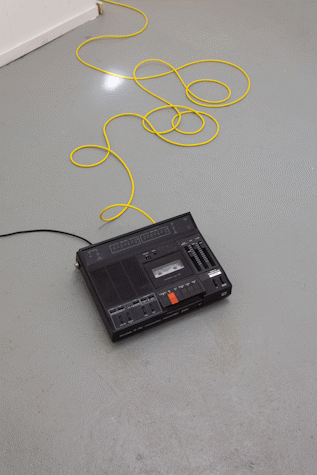 tape recorder on a grey floor with a yellow wire extending from it