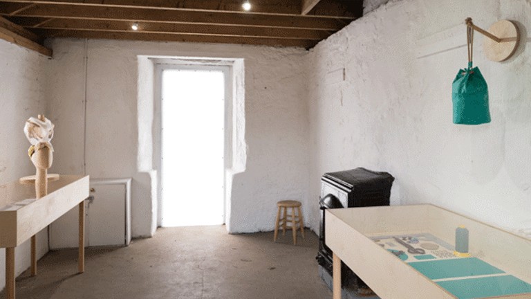 View of an exhibition space with an open door at the end. Vitrines are shown on either side, containing exhibition material. A stove is also visible. 