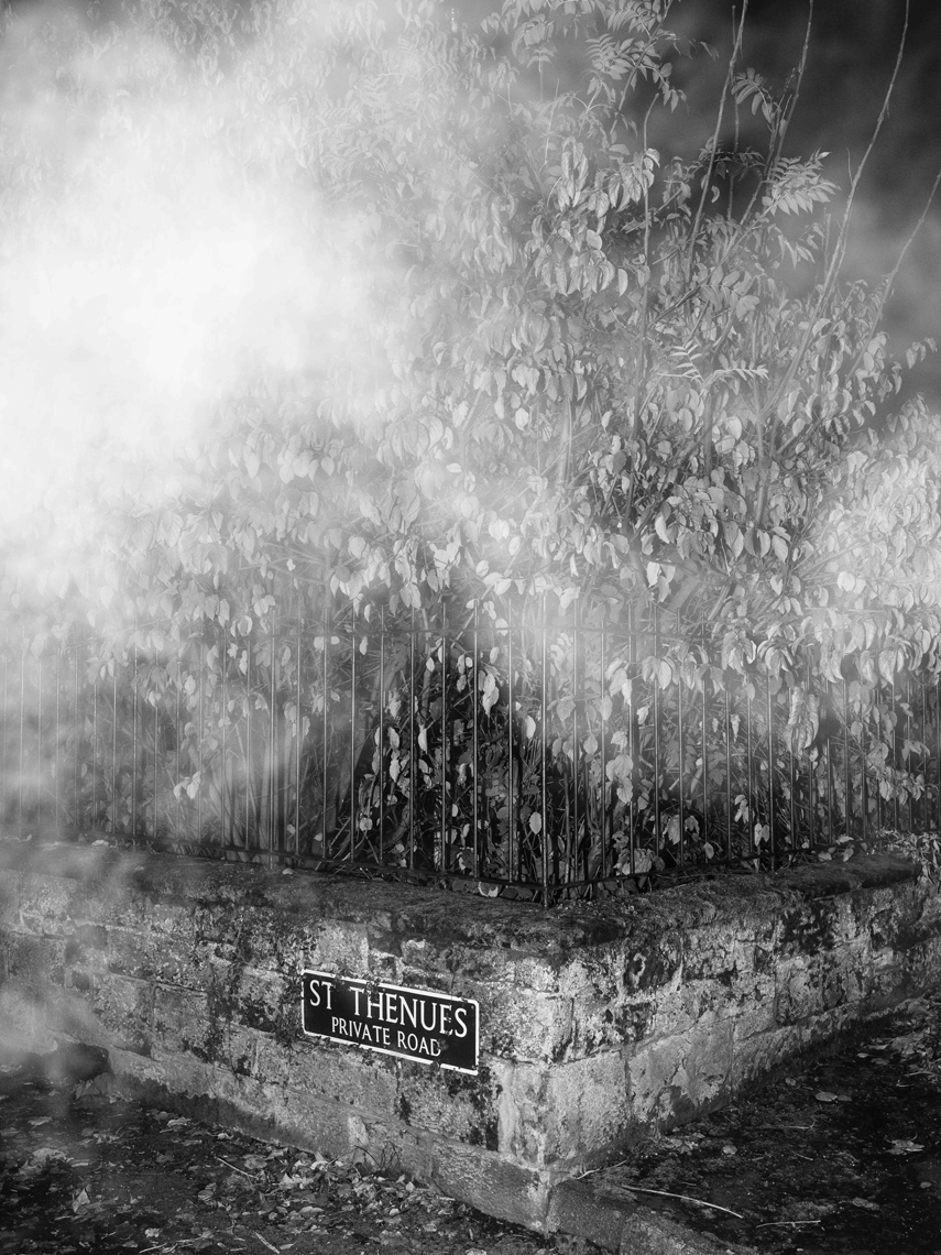 black and white image of a street corner with a street sign reading 'St Thenues Private Road'