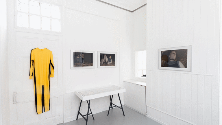  Yellow jumpsuit hung on door, framed photographs on gallery wall