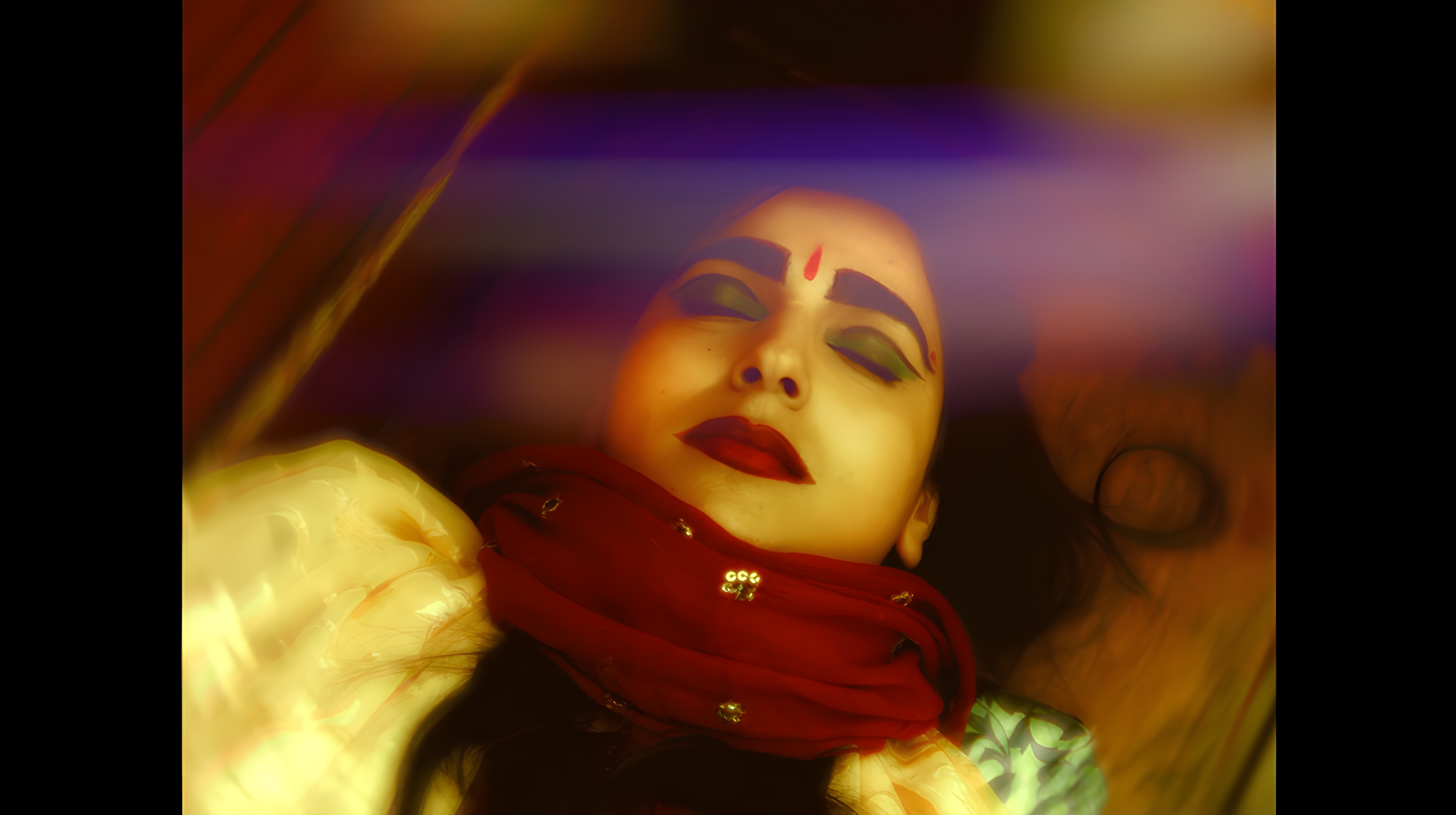 A portrait of a woman with a calm and serene expression. She is lying down, adorned with bold makeup, including dramatic eye makeup with green and black hues and a red scarf wrapped around her neck. A red teardrop bindi is visible on her forehead. The soft lighting and subtle blurring around the edges of the image create a dreamlike and ethereal quality, the mood feels contemplative, as if she is in a moment of quiet introspection or meditation.
