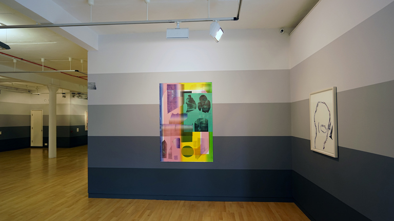 Art gallery with wooden floors and horizontally stripes in the walls in a gradiant from black to white from bottom to top. We see a colourful printed painting in purple, pink, blue green, yellow and black. To the right a white print. 